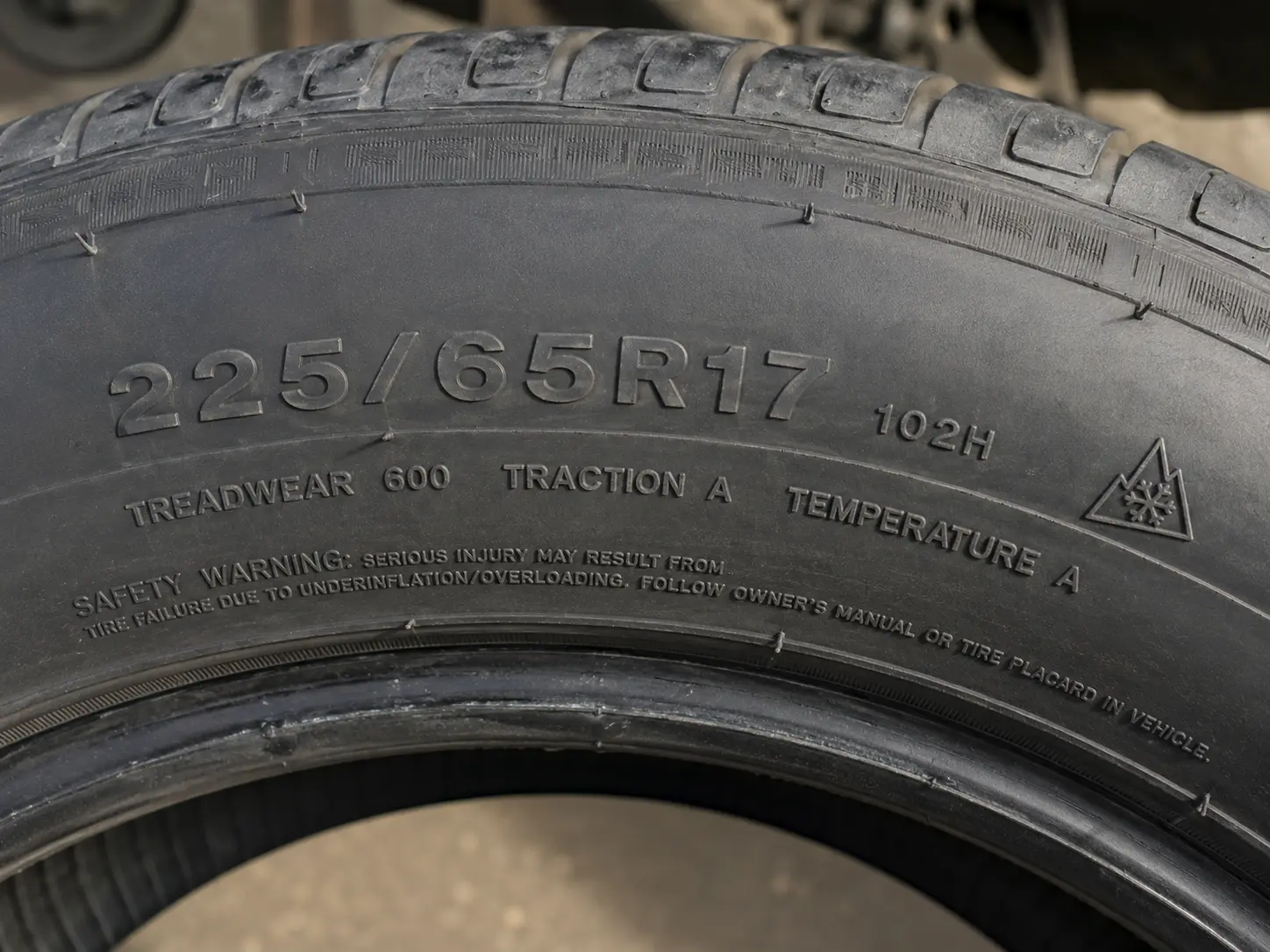 Close-up of tire sidewall showing 225/65R17 size marking, UTQG treadwear rating, and 3PMSF snowflake 