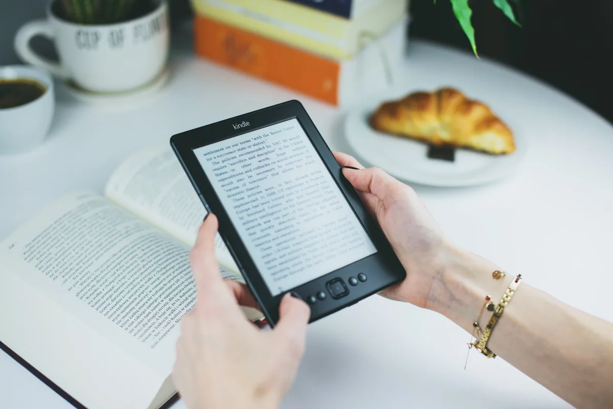 Woman holding a Kindle e-reader at a café table with a croissant