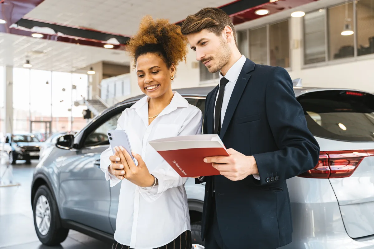 Couple reviewing car options on smartphone at a dealership in 2026