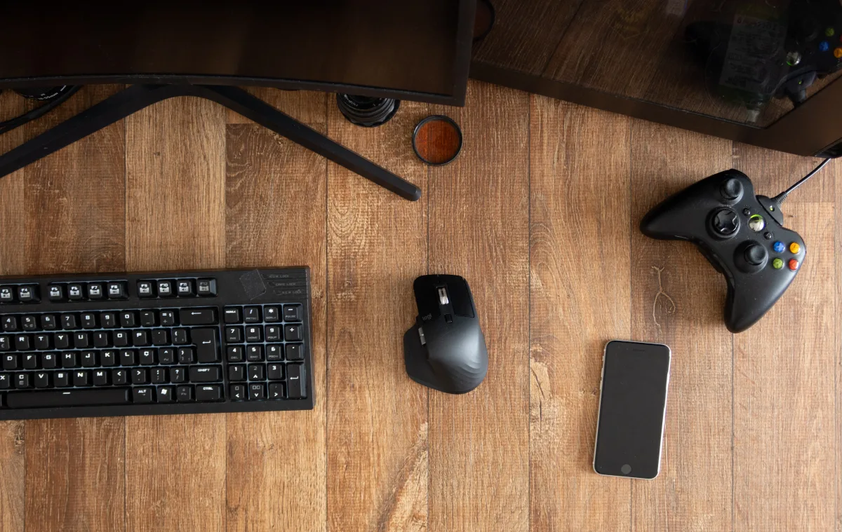 Top-down view of a gamepad, mouse, and keyboard on a wooden desk beside a monitor