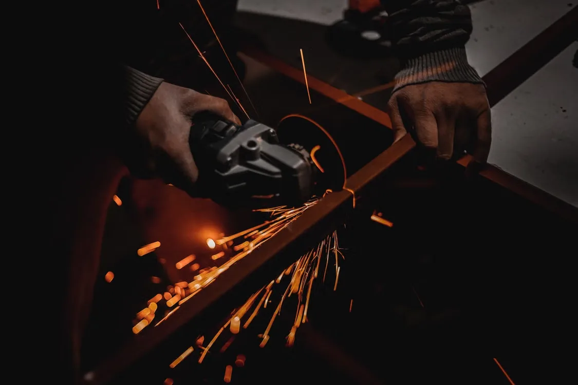 Worker using an angle grinder with sparks flying in a dark workshop