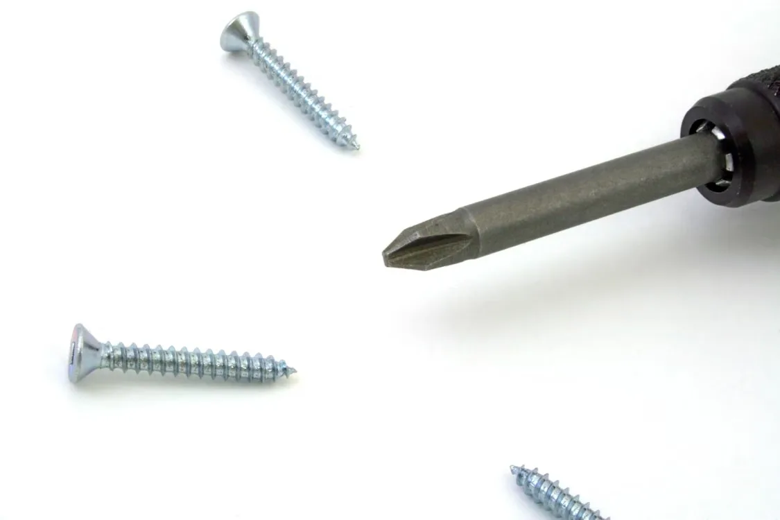 Detailed view of a screwdriver with screws scattered on a white surface
